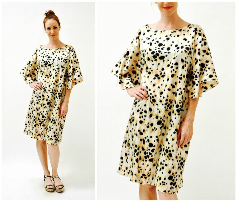 May include: A short-sleeved dress with a beige background and a black and brown animal print. The dress has a round neckline and a loose fit. The sleeves are ruffled and end at the elbow.