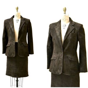 May include: A brown suede suit jacket and skirt set. The jacket has a single button closure and two pockets. The skirt is a-line and hits just above the knee.