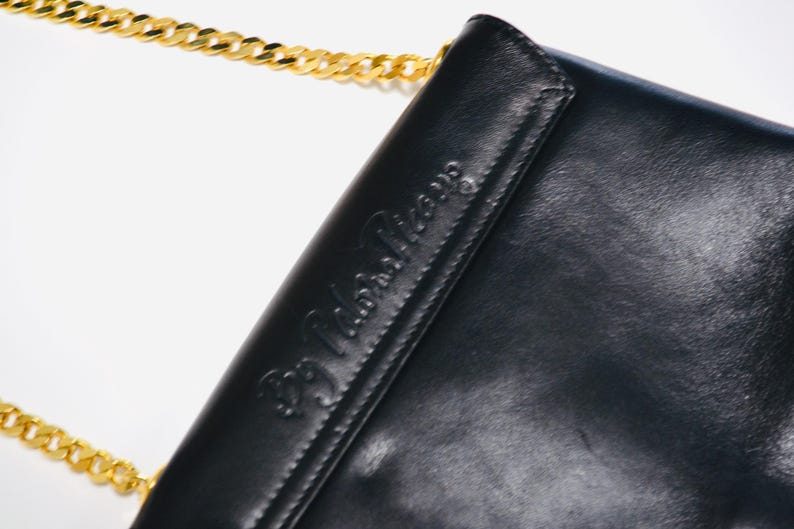May include: Black leather shoulder bag with a gold chain strap and the embossed text "BB John Paris".