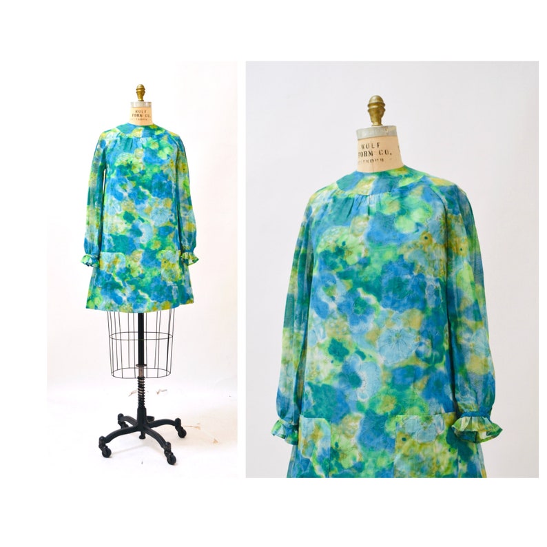 May include: A vintage 1960s mod dress with a blue and green abstract print. The dress has long sleeves with ruffles at the cuffs and a loose, A-line silhouette.
