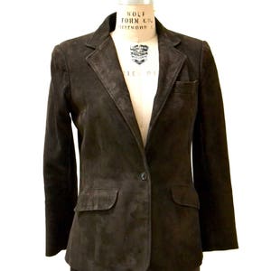 May include: A brown suede blazer and skirt suit. The blazer has a single button closure and two flap pockets. The skirt is knee-length.