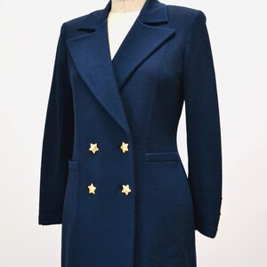 May include: A navy blue double-breasted blazer with gold star buttons. The blazer has a long, fitted silhouette and is made of a soft, textured fabric.