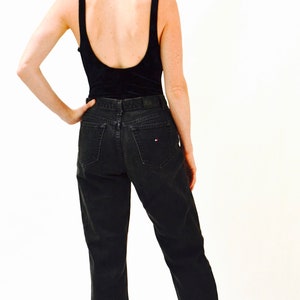 May include: A woman wearing a black tank top and black jeans with a small red and white logo on the back pocket. She is wearing black sandals with a gold platform.