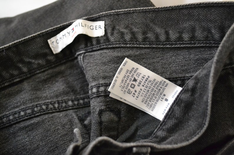 May include: A black Tommy Hilfiger jeans label with care instructions and size information. The label reads "1% COTTON COTON ALGODON", "MADE IN MEXICO OF US FABRIC", "FABRIQUE AU MEXIQUE AVEC TISSUS DES ETATS-UNIS", "HECHO EN MEXICO CON TELA DE EEUU.", "#66476 #20781", "187369 #47", "WASH AND DRY INSIDE OUT", "WASH SEPARATELY", "DRY PROMPTLY", "OVER VERSO AL REVERSO", "KTYKTY", "R/31", "8".