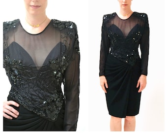 May include: A black sequined evening dress with a sheer overlay and long sleeves. The dress has a fitted bodice and a flowing skirt.