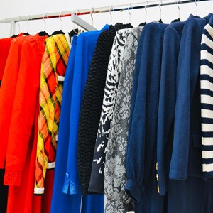 May include: A rack of clothing with a variety of colors and patterns, including red, blue, black, white, and yellow. The clothing includes sweaters, shirts, and dresses.