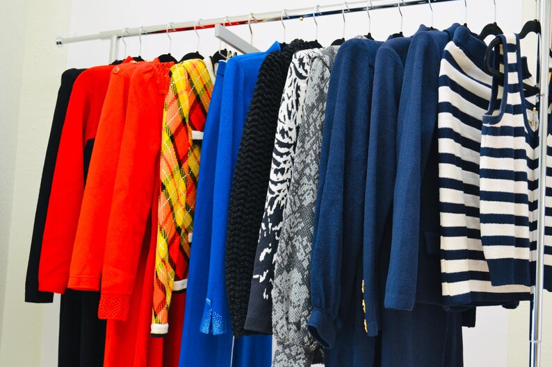 May include: A rack of clothing with a variety of colors and patterns, including red, blue, black, white, and yellow. The clothing includes sweaters, shirts, and dresses.