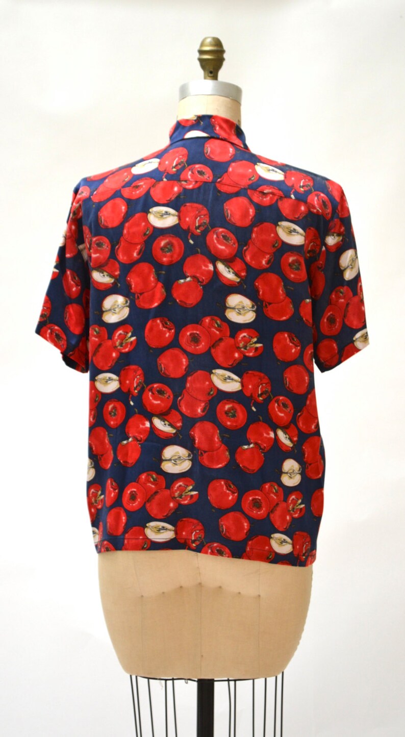 May include: A navy blue short-sleeved shirt with a red apple print.