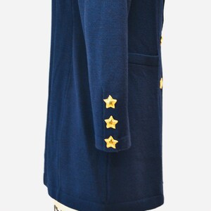 May include: A navy blue long-sleeved coat with gold star buttons on the cuffs. The coat is on a mannequin.
