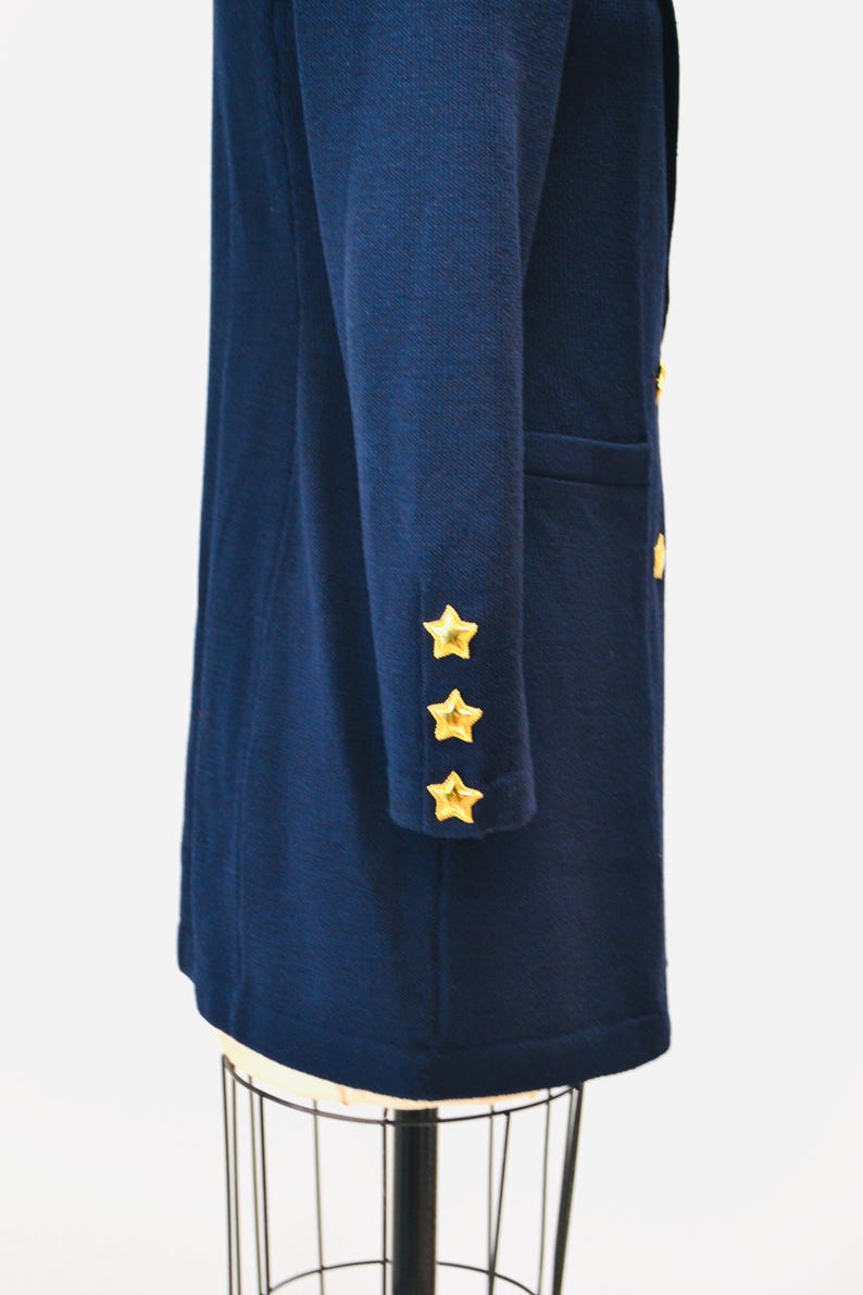 May include: A navy blue long-sleeved coat with gold star buttons on the cuffs. The coat is on a mannequin.