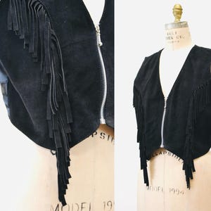 May include: A black suede vest with fringe detailing and a zipper closure. The vest is cropped and has a v-neck.