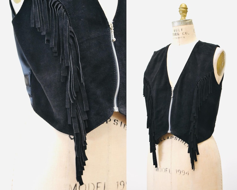 May include: A black suede vest with fringe detailing and a zipper closure. The vest is cropped and has a v-neck.