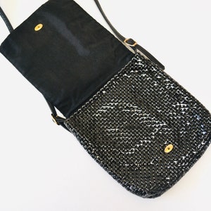 May include: A black chainmail crossbody bag with a flap closure and a gold-toned clasp. The bag has a black fabric lining and a long adjustable strap.