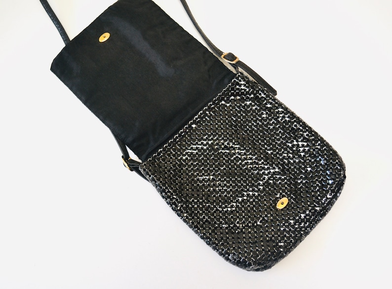 May include: A black chainmail crossbody bag with a flap closure and a gold-toned clasp. The bag has a black fabric lining and a long adjustable strap.