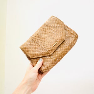 May include: A brown snakeskin clutch purse with a gold clasp.