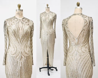 May include: A long, silver sequined gown with long sleeves and a high neckline. The dress features intricate sequin patterns and a keyhole back. The gown is displayed on a dress form.