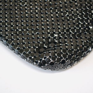 May include: Close-up of a black mesh bag with a shiny finish. The mesh is made of small, round, interconnected metal pieces.