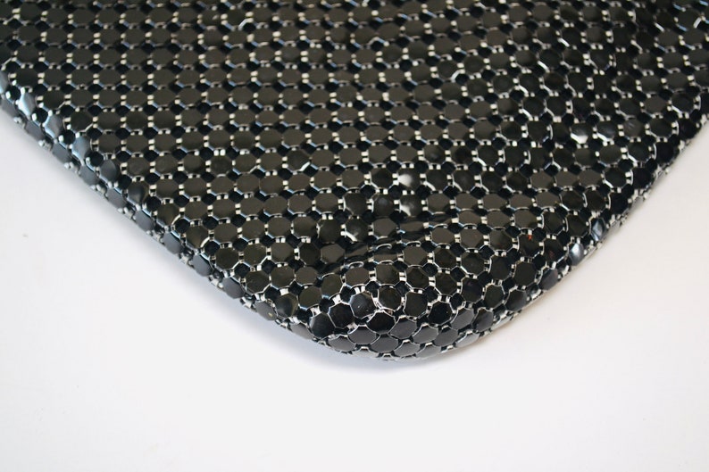 May include: Close-up of a black mesh bag with a shiny finish. The mesh is made of small, round, interconnected metal pieces.
