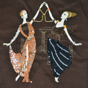 May include: Brown fabric featuring an embroidered design of two figures in flowing gowns, decorated with sequins and jewellery. They are holding hands, with a gold chain between them. A classical architectural backdrop is in the background.