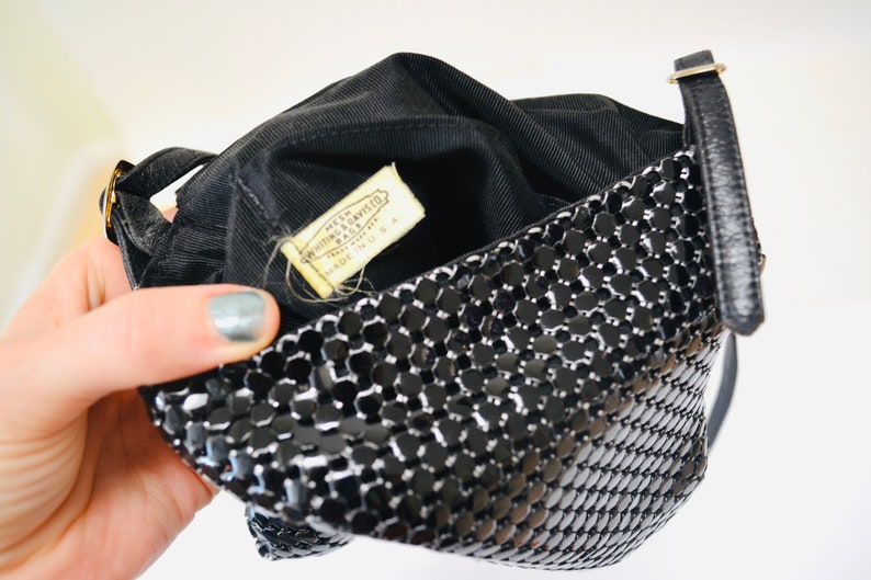 May include: Black mesh purse with a gold chain strap and a label that reads "Made in USA" by "Whitting & Davis, Inc."