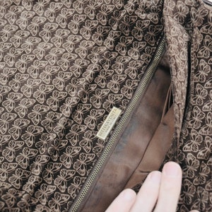 May include: The inside of a brown leather handbag with a butterfly pattern. The bag has a zipper closure and a label that reads "Bottega Veneta Made in Italy".