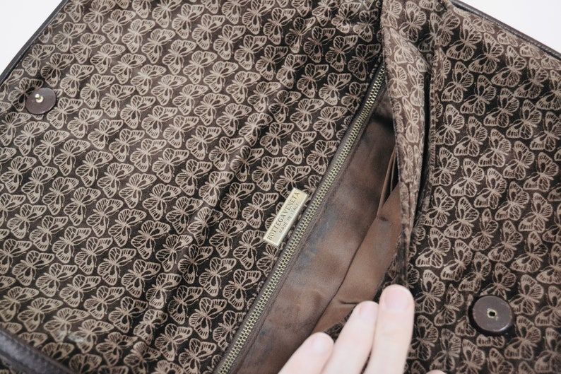 May include: The inside of a brown leather handbag with a butterfly pattern. The bag has a zipper closure and a label that reads "Bottega Veneta Made in Italy".
