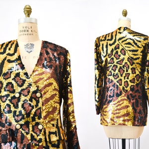 Puede incluir: Una chaqueta de lentejuelas dorada, marrón y negra con estampado de leopardo, cebra y tigre. La chaqueta tiene cierre de doble botonadura con botones dorados.