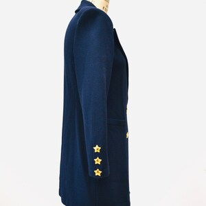 May include: A navy blue blazer with gold star buttons on the sleeves. The blazer is on a mannequin and has a double-breasted closure.