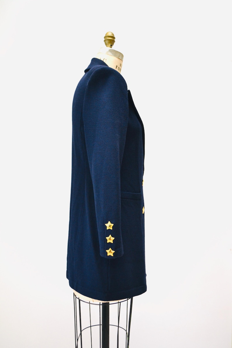 May include: A navy blue blazer with gold star buttons on the sleeves. The blazer is on a mannequin and has a double-breasted closure.