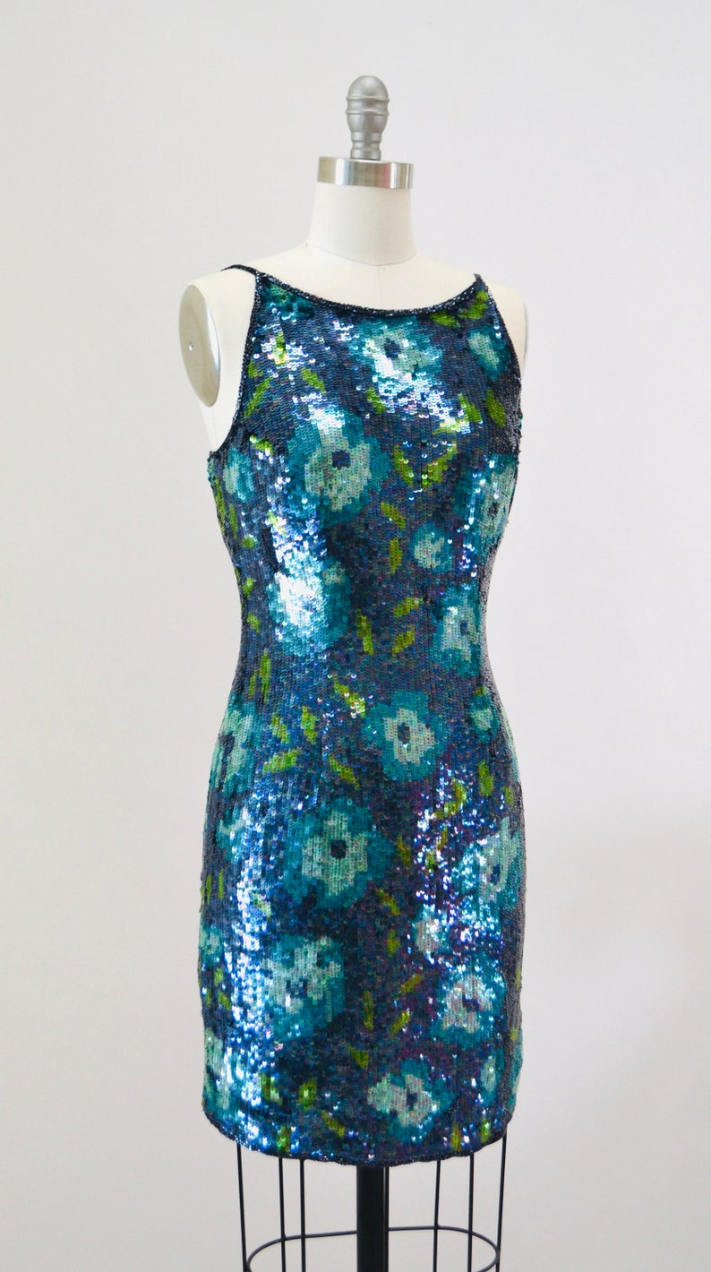 May include: A sleeveless sequined dress with a floral pattern in shades of blue and green.