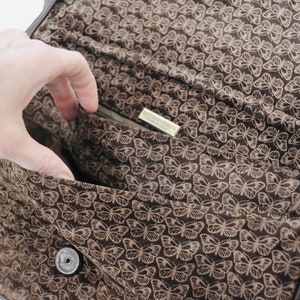 May include: The inside of a brown leather bag with a butterfly print lining. The bag has a zipper closure and a small metal tag that reads "Nine West".