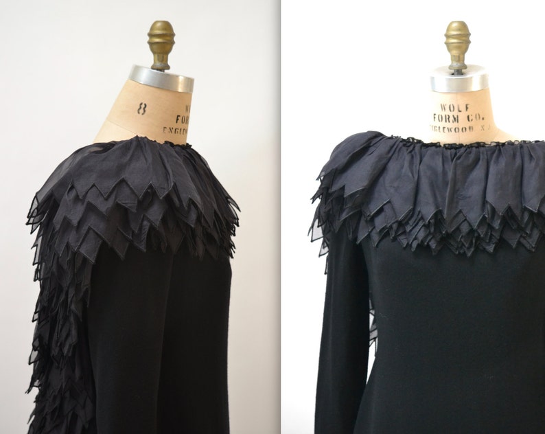 May include: A black long-sleeved dress with a large, layered ruffle collar. The ruffle is made of sheer fabric and has a scalloped edge.