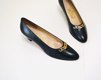 May include: A pair of black leather pumps with gold chain detailing. The shoes have a pointed toe and a low heel.