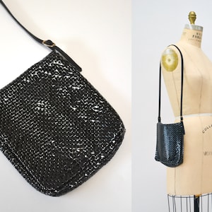 May include: A black chainmail shoulder bag with a long adjustable strap. The bag is made of small metal rings that are linked together.