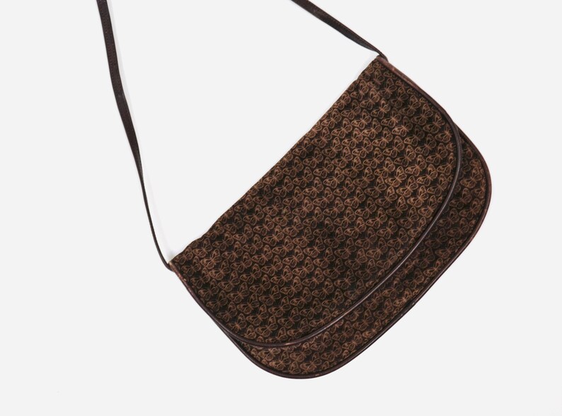 May include: A brown leather shoulder bag with a butterfly pattern. The bag has a long strap and a flap closure.