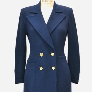 May include: A navy blue blazer with a double breasted closure and gold star buttons. The blazer has a long sleeve and a fitted silhouette.