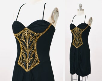 May include: A black sleeveless dress with a gold sequined bodice. The bodice features a geometric design with a pointed shape at the bottom.