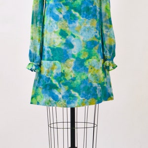 May include: A blue and green tie-dye dress with a round neckline and long sleeves. The dress is on a dress form with a black metal stand.