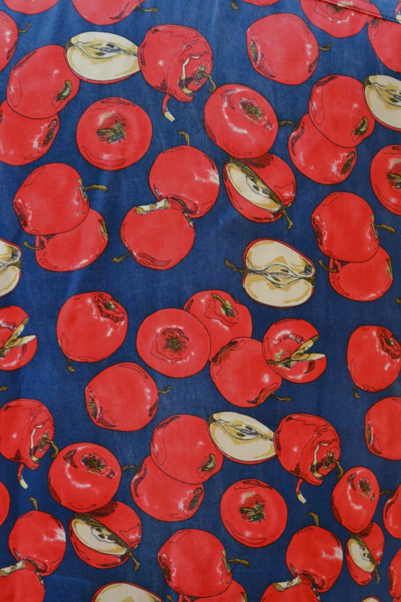 May include: A blue fabric with a repeating pattern of red apples. The apples are drawn in a realistic style with some showing a cross-section of the fruit.