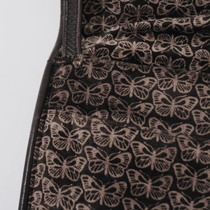 May include: Close-up of a black leather bag with a brown butterfly pattern lining.