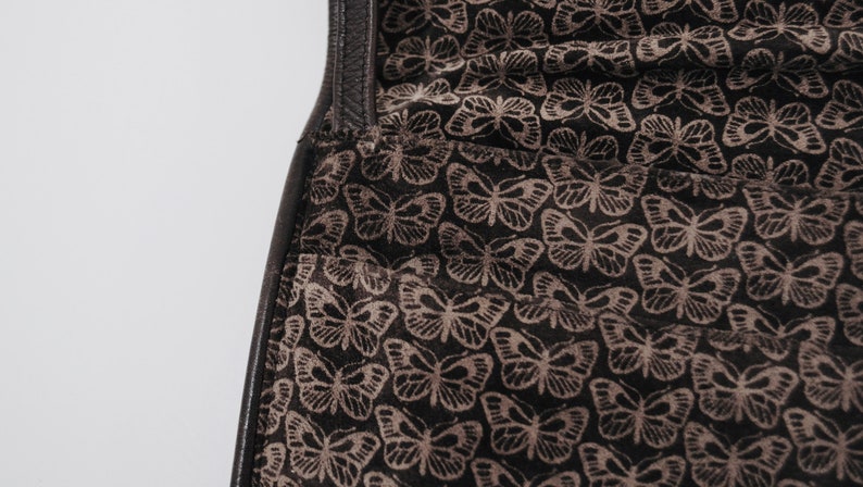May include: Close-up of a black leather bag with a brown butterfly pattern lining.