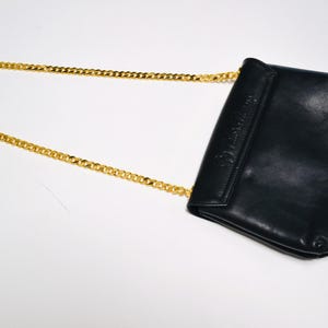 May include: A black leather shoulder bag with a gold chain strap. The bag has a flap closure and a small pocket on the front.