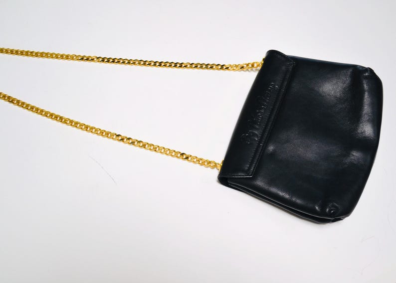 May include: A black leather shoulder bag with a gold chain strap. The bag has a flap closure and a small pocket on the front.