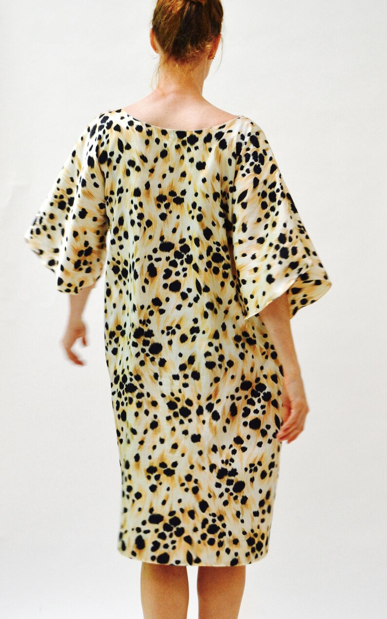 May include: A white dress with a black and brown animal print. The dress has a loose fit and a scoop neck.