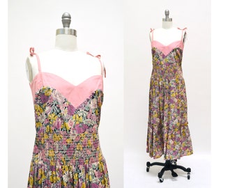 May include: A pink and floral print sundress with thin straps and a gathered skirt. The dress has a pink bodice with a sweetheart neckline.