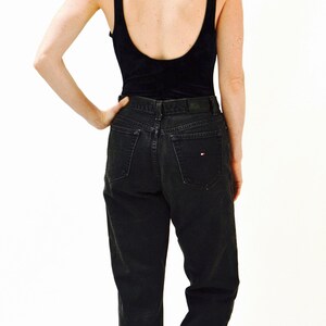 May include: A woman wearing a black tank top and black jeans with a small red and white logo on the back pocket. She is wearing black sandals with a platform.