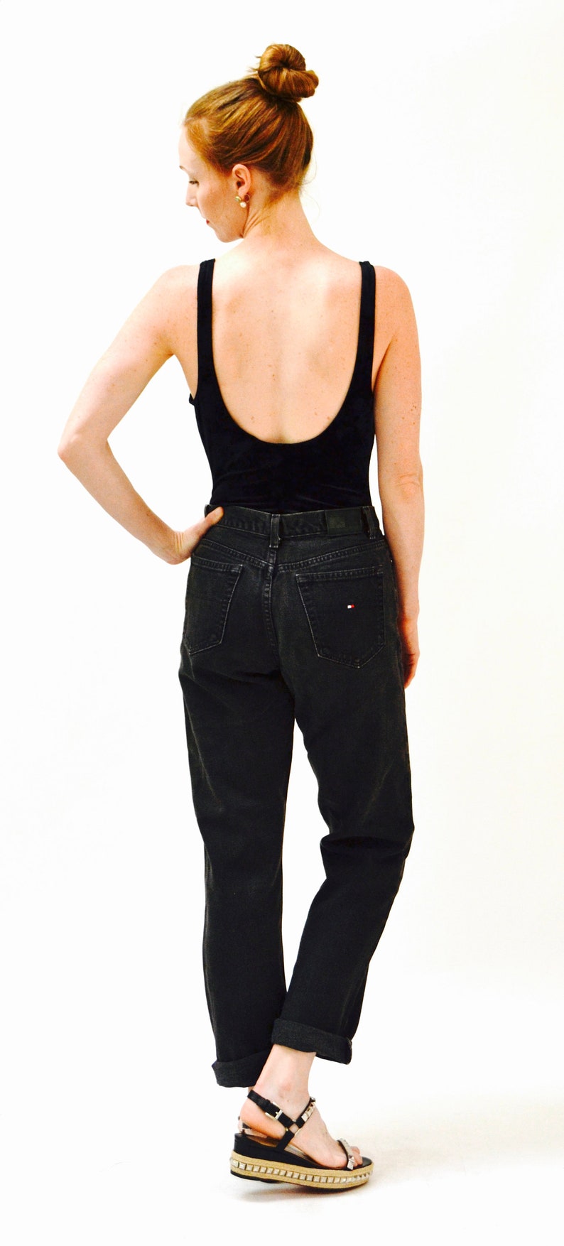 May include: A woman wearing a black tank top and black jeans with a small red and white logo on the back pocket. She is wearing black sandals with a platform.