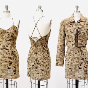 Op de afbeelding: Een tweedelige outfit met een bruine en zwarte tijgerprint. De outfit bestaat uit een mouwloze minirok met een gekruiste rug en een kort jack met knoopsluiting.