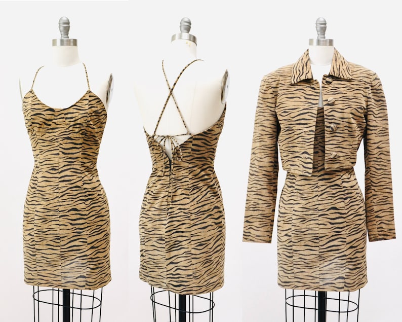 Op de afbeelding: Een tweedelige outfit met een bruine en zwarte tijgerprint. De outfit bestaat uit een mouwloze minirok met een gekruiste rug en een kort jack met knoopsluiting.