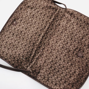 May include: A brown leather shoulder bag with a butterfly pattern lining. The bag has a flap closure and a long strap.